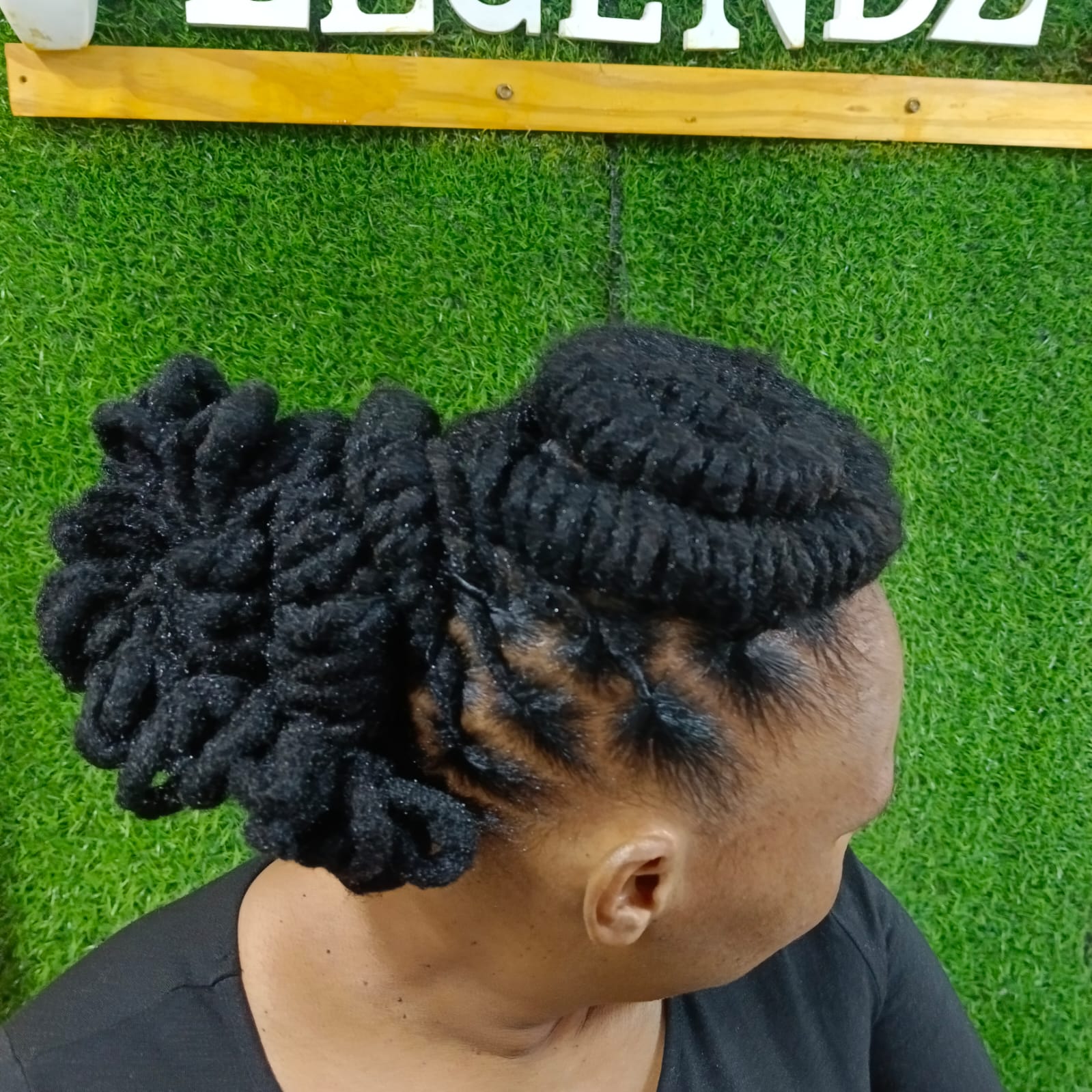 Locs styled into a sculpted updo with twisted sides, in front of the Legendz sign